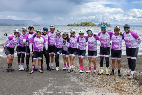 Cyclists in white and purple jerseys and black shorts posing on a beach in Chile