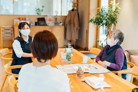 Three japanese women wearing masks sit at a table, with smiles