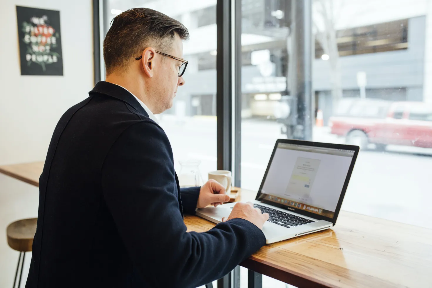 Man working on a laptop computer on a high table in front of a brightly lit window