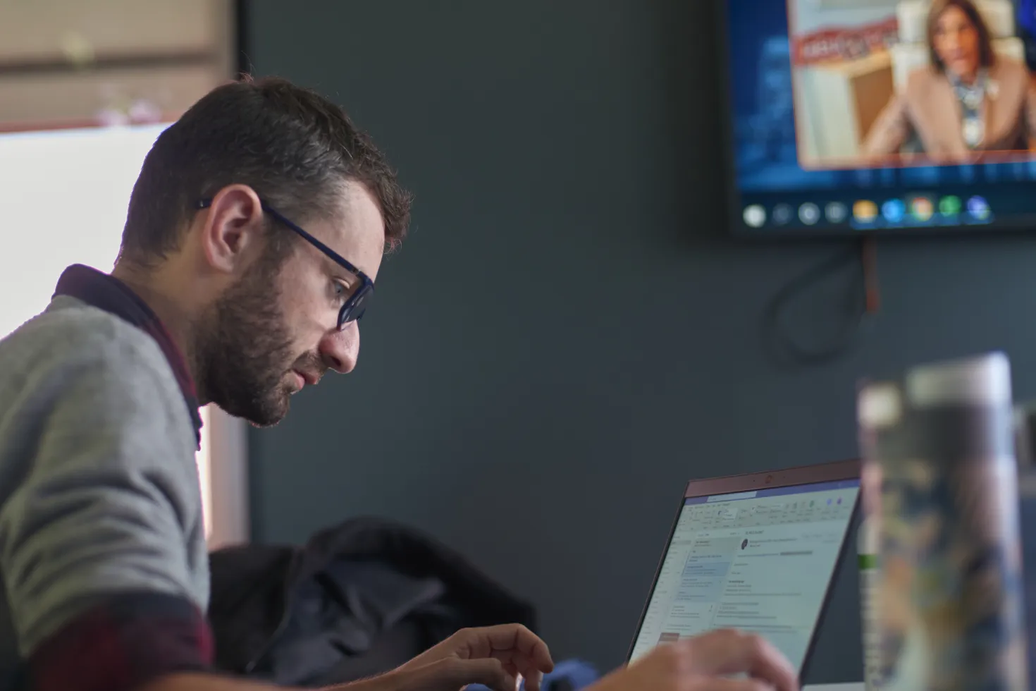 Young man looking at laptop computer with conference screen in background