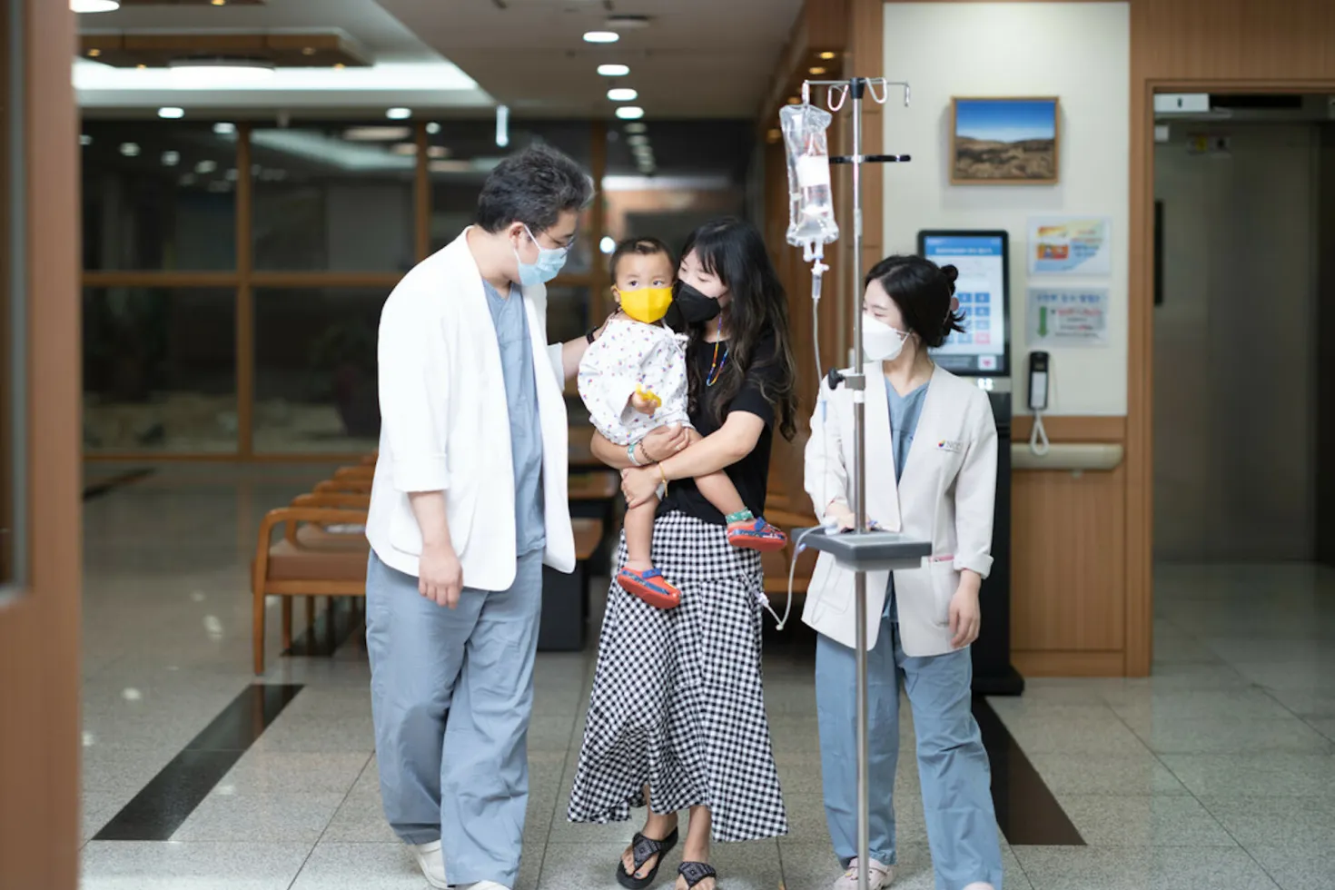 A male and female doctor accompany a woman carrying her young child in hospital ward