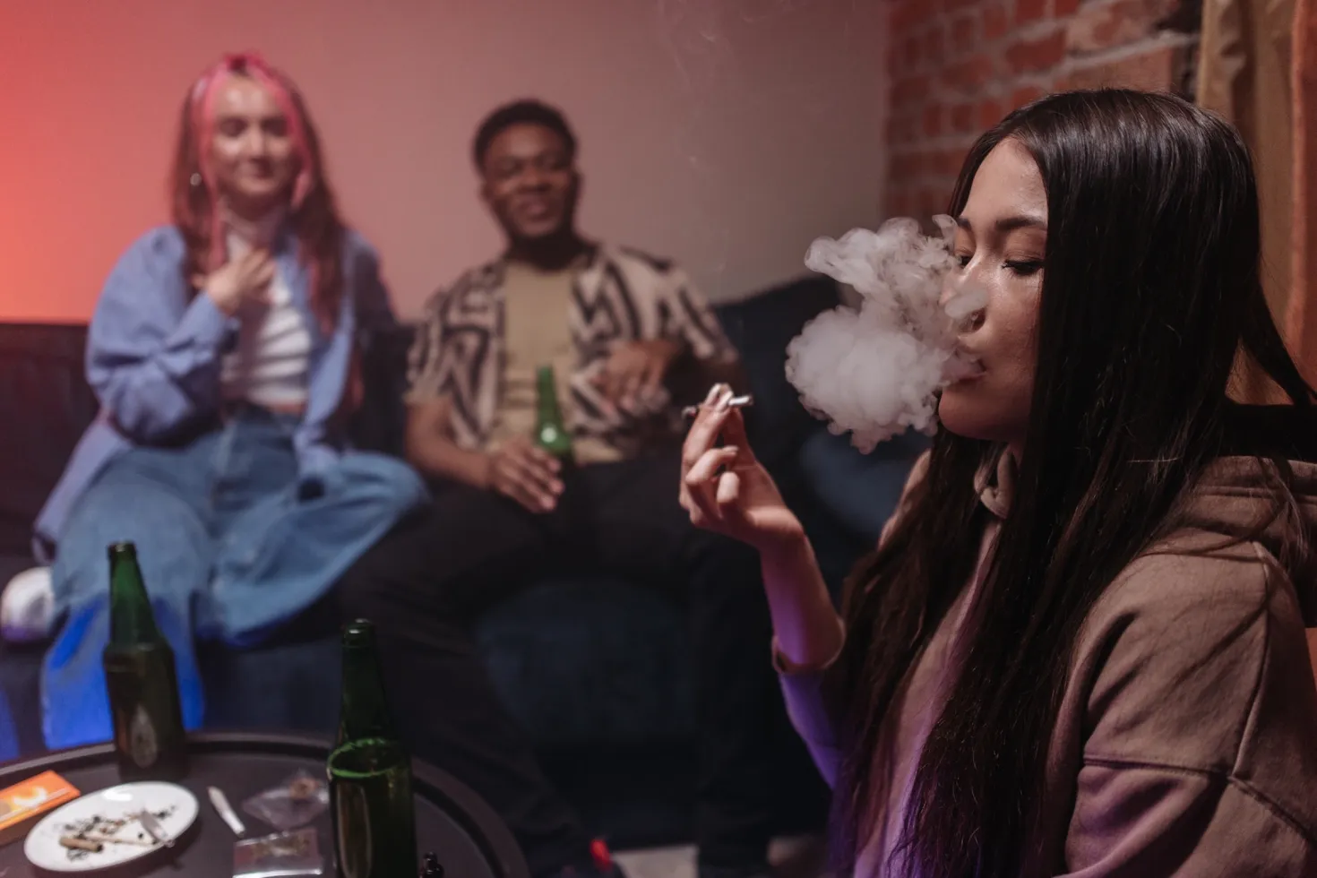 Two women and a man at a party drinking and smoking