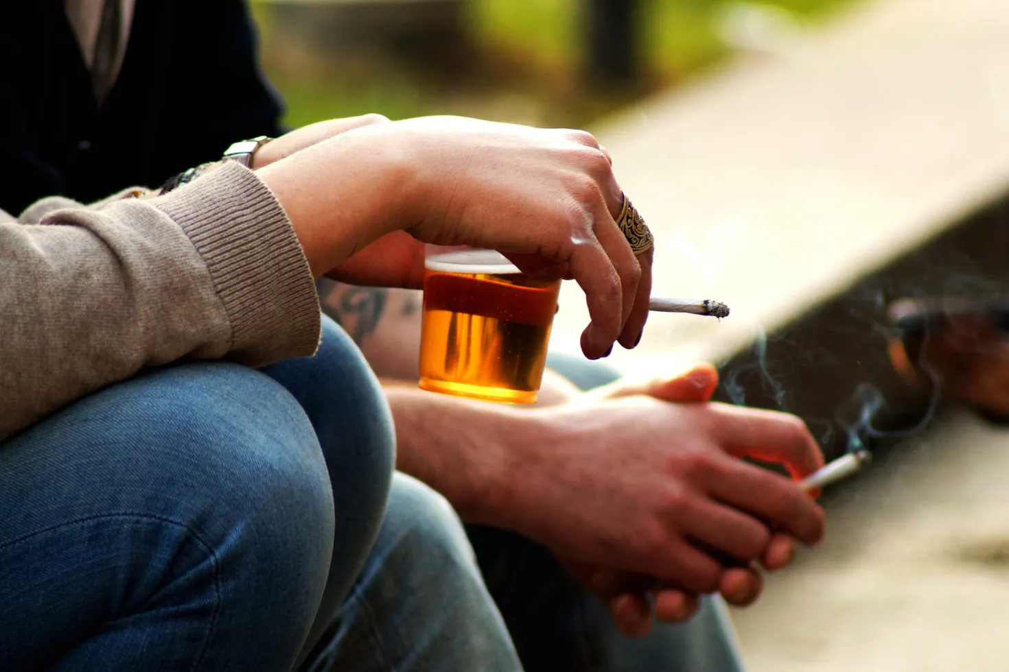 Hands of a man and a woman holding a glass of alcohol and cigarettes