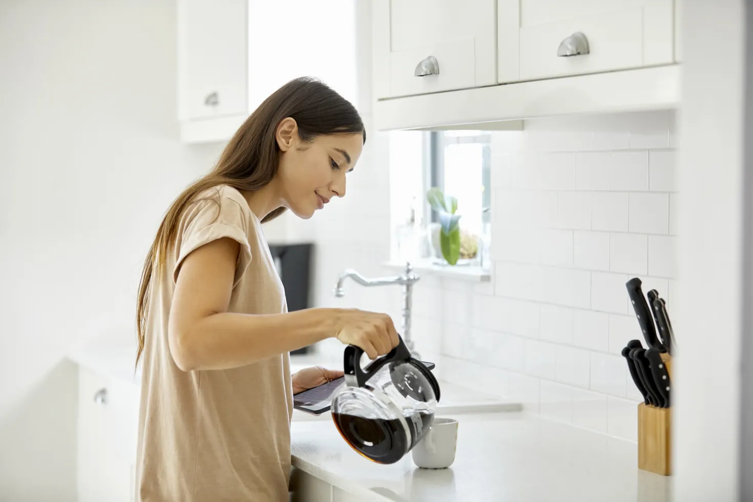 Woman with long dark hair serving a cup of coffee from a pot