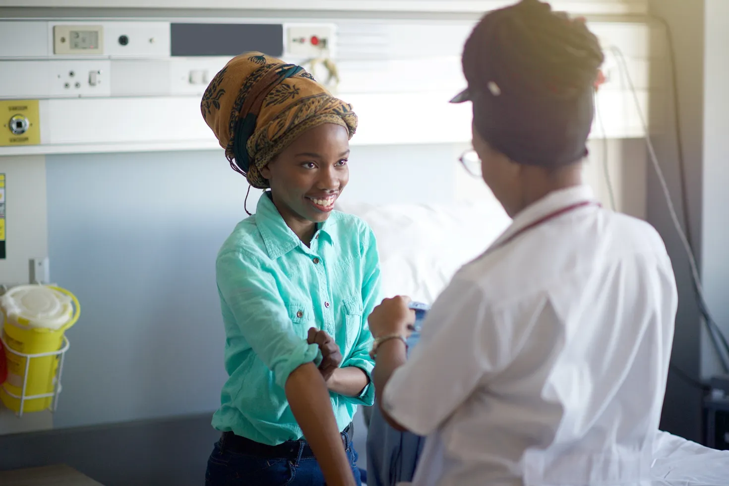African nurse seen from behind taking the blood pressure of a young African girl wearing a turquoise shirt, smiling