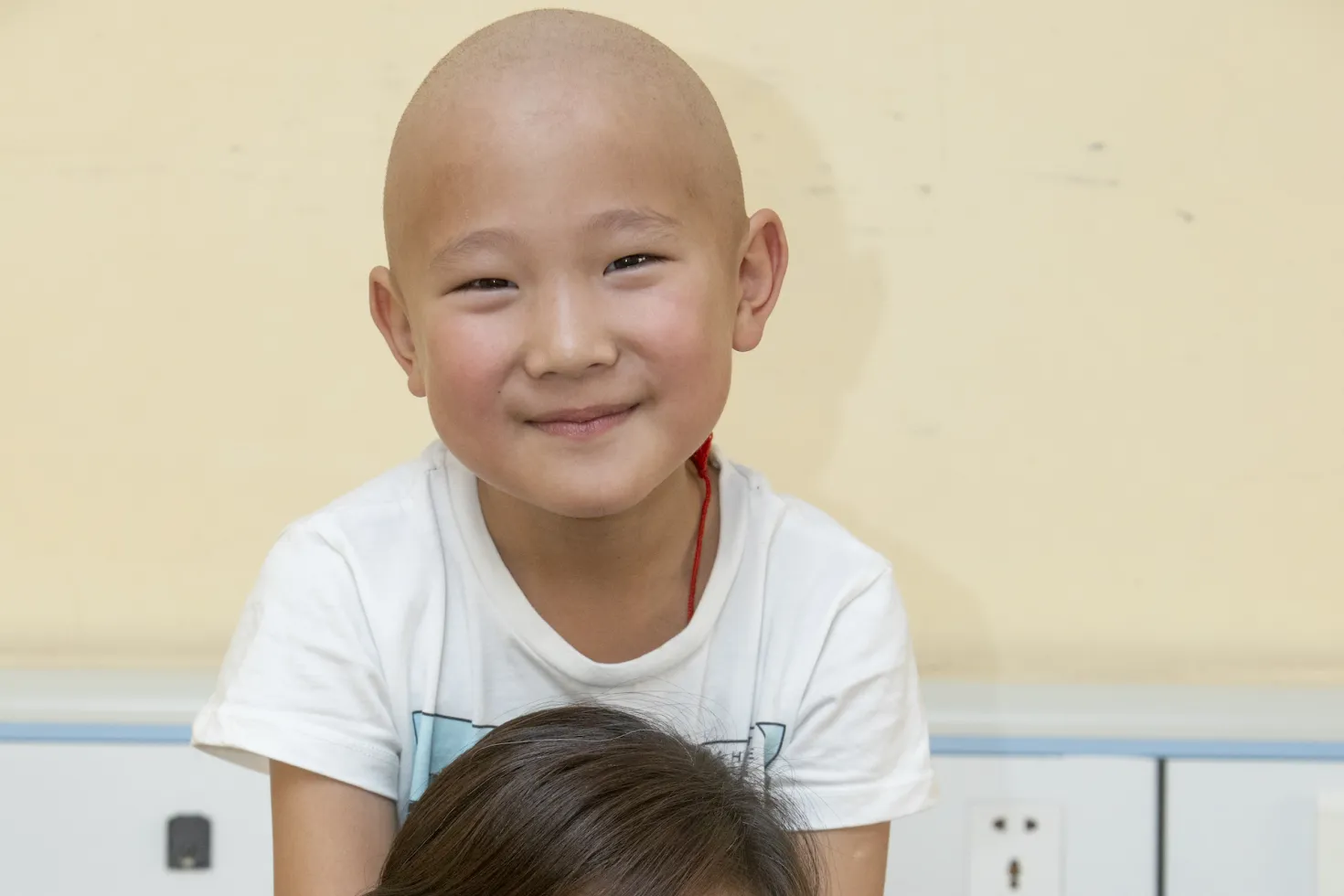 Woman with dark hair in Mongolia with a bald child, cancer patient, on her shoulders