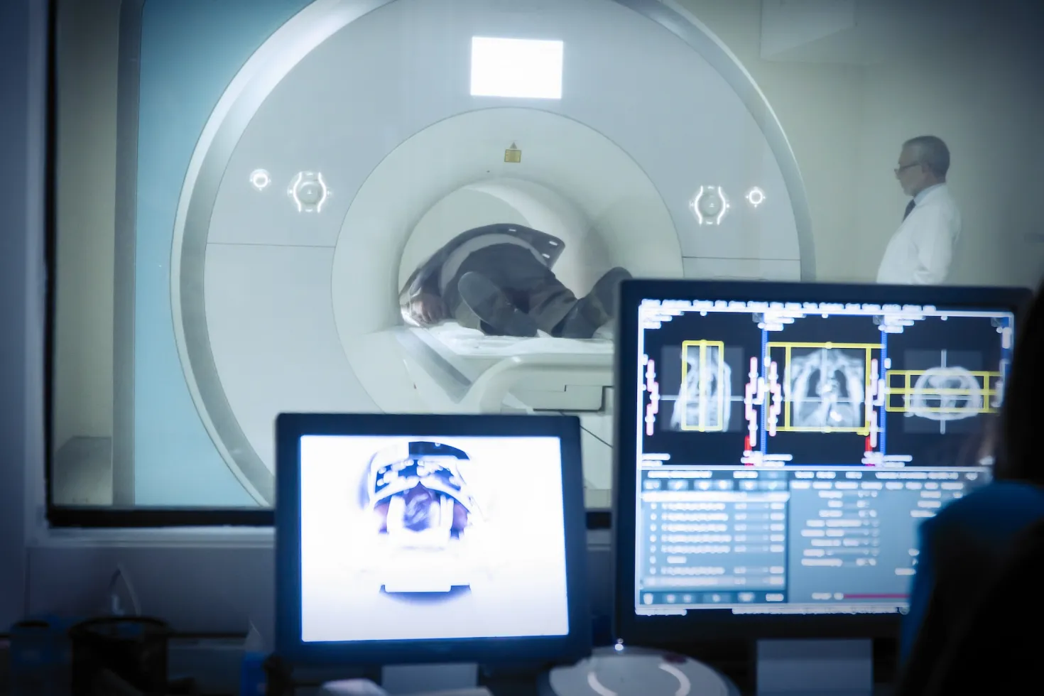In the background, man having a CT scan. In foreground, computer screens displaying the scans.