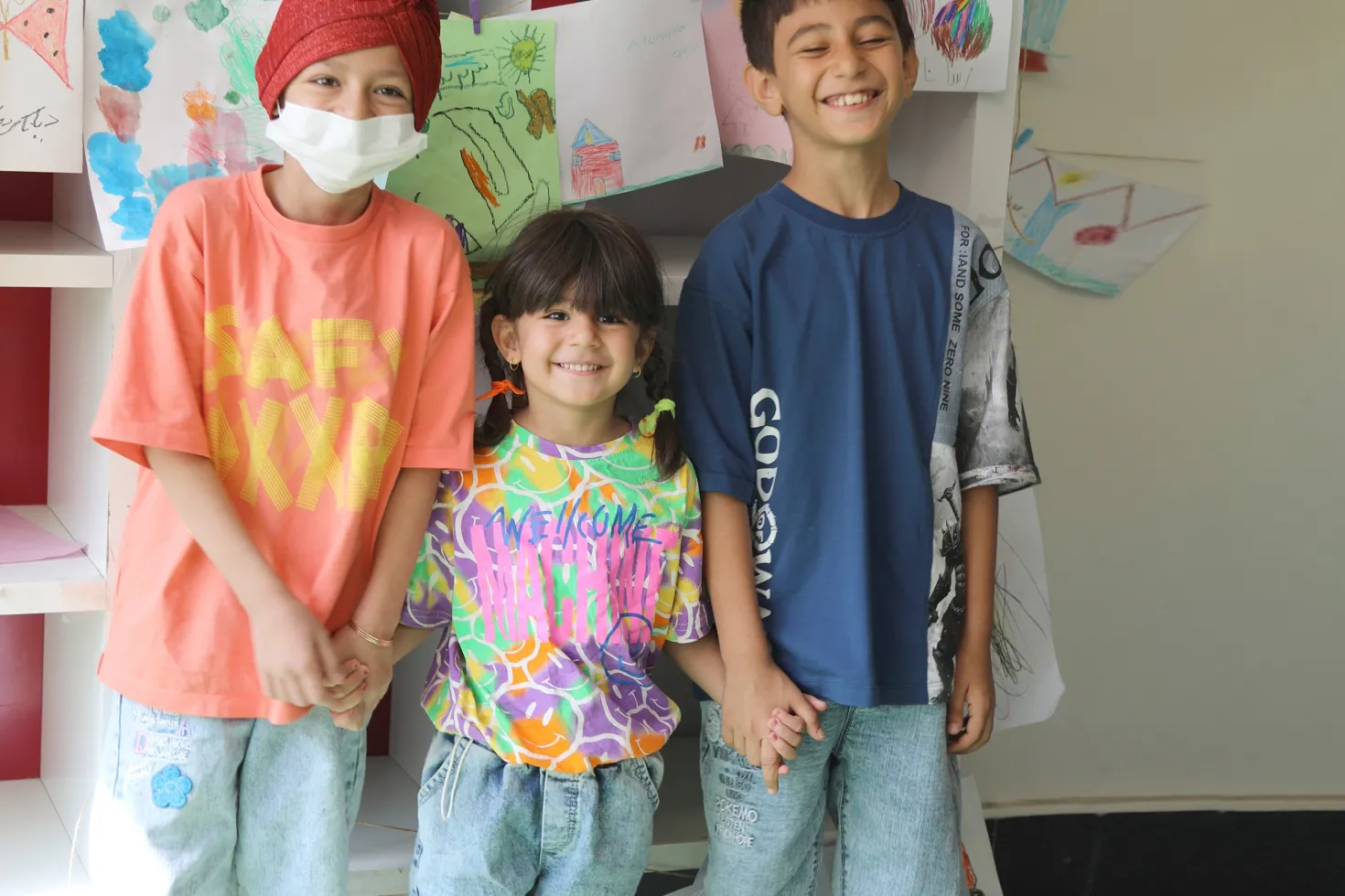 Three children in colorful shirts, one wearing a mask, in a cancer centre for children