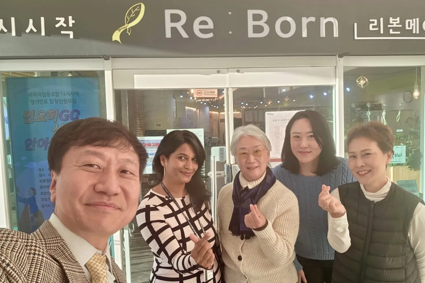 Diverse group featuring one man and four women posing for a picture in front of a sign "Re:Born"