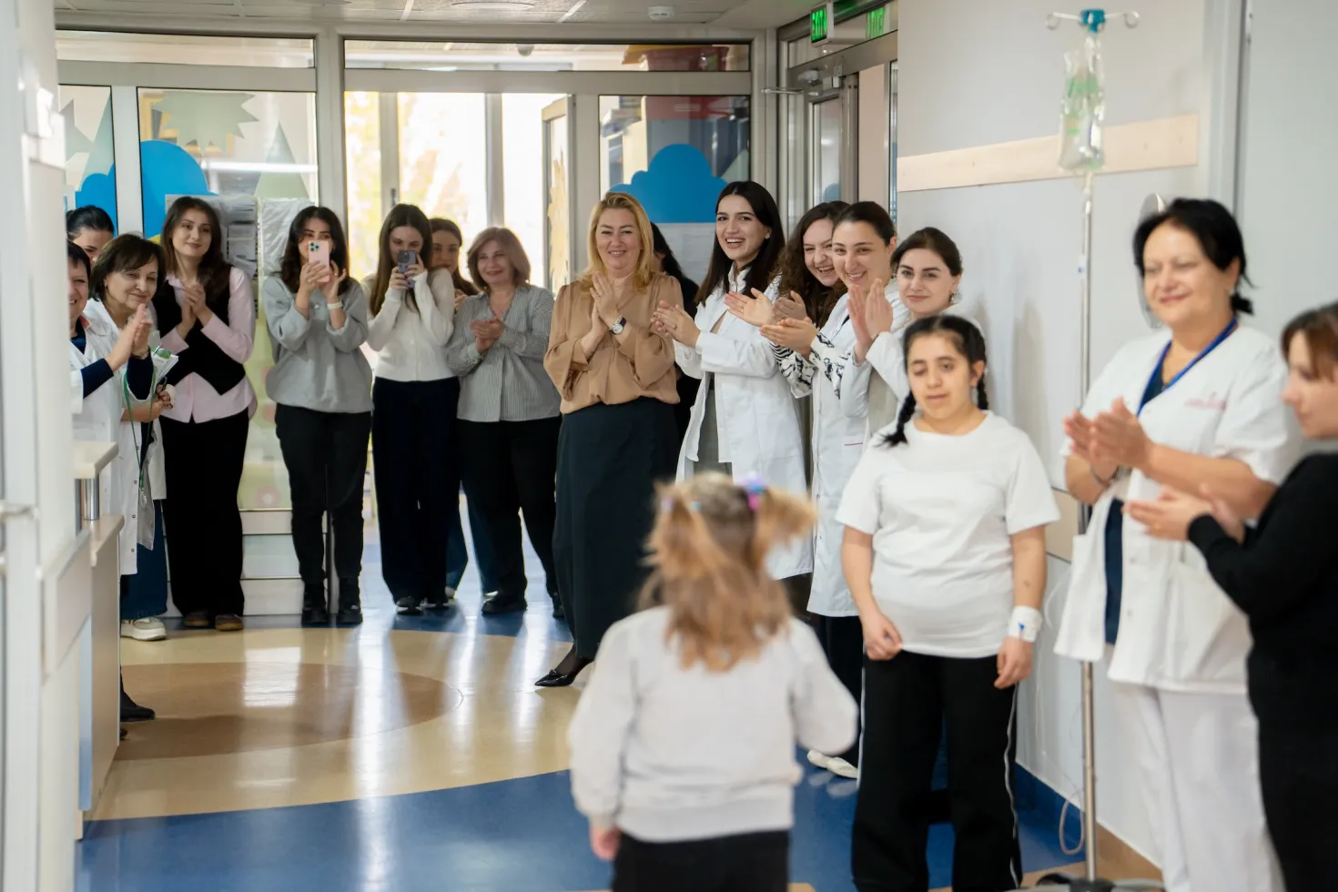 A child with cancer is cheered by the clinicians and health workers as she walks down the hall to ring the remission bell