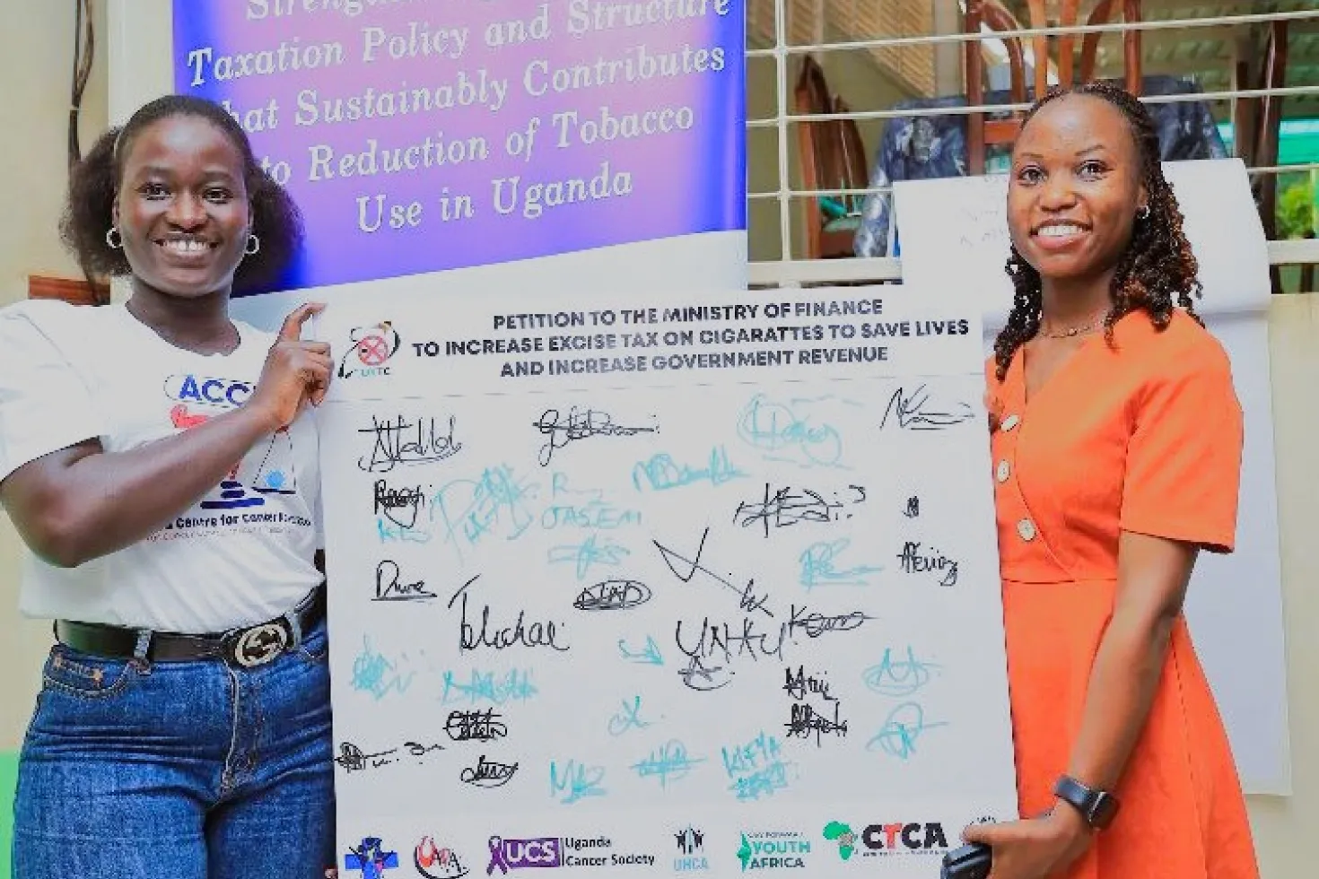 Two young Black women holding a board of signatures for a tobacco taxation campaign in Uganda