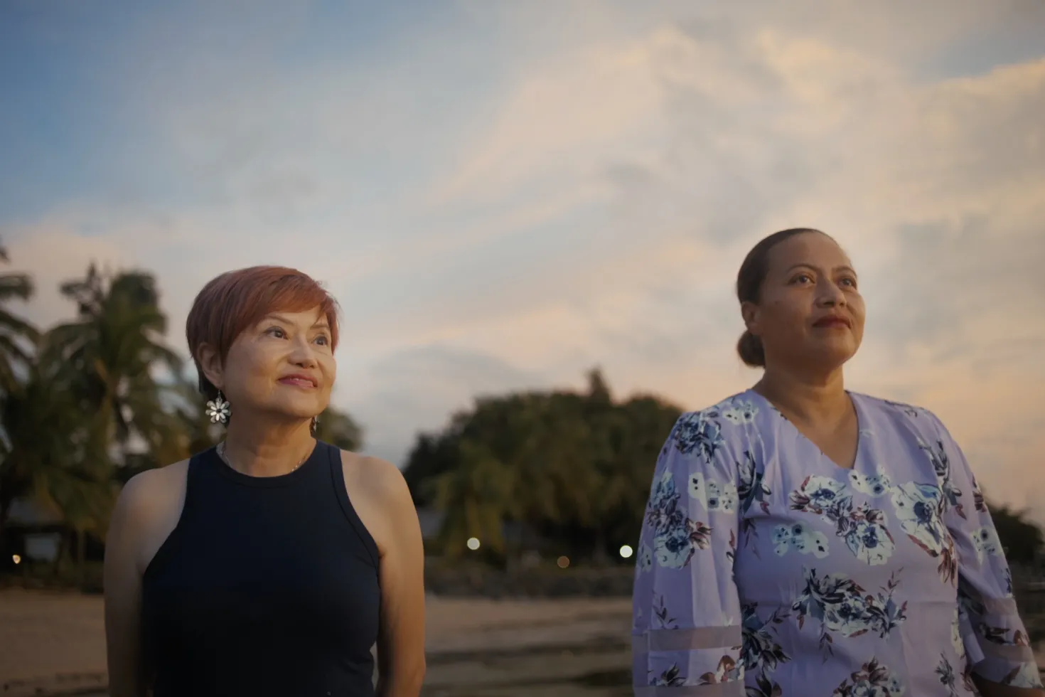 Two women standing outside and smiling with a beautiful blue sky and tree behind them