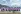 Group of cyclists from Japan in BMS branded pink shirts facing Mount Fuji with arms raised, backs to the camera