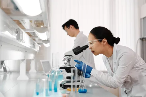 Women in a lab using a microscope, with a man in the background studying a sample