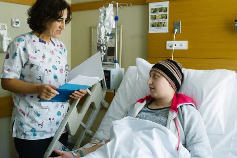 Women healthcare provider talking to a cancer patient lying in a hospital bed, holding a file in her hands