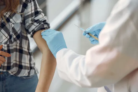 Close-up of a medical practitioner wearing blue surgical gloves preparing a woman's arm for an injection