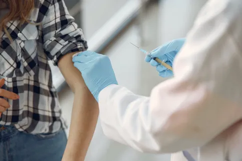Close-up of a medical practitioner wearing blue surgical gloves preparing a woman's arm for an injection