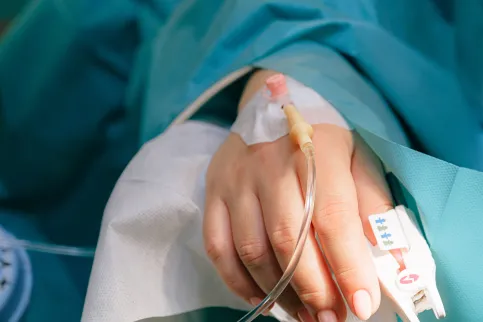 Close up of IV drip in a white hand lying on a hospital bed