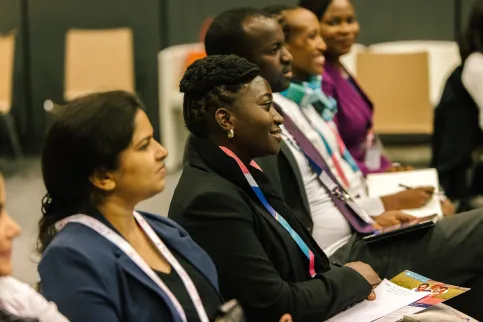 A diverse group of people sitting at individual desks listening to a presentation