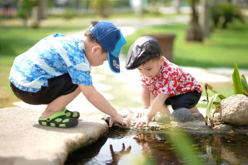 Two Asian children playing by a stream in a park