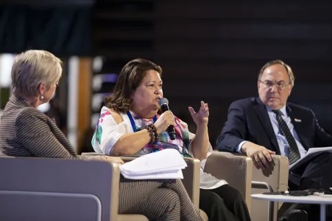Carmen Auste, CEO of Cancer Warriors Philippines speaking at a conference panel with two men on either side of her