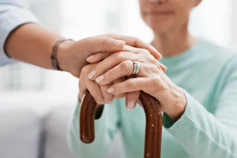 A young white hand clasping an older white hand resting on top of a cane
