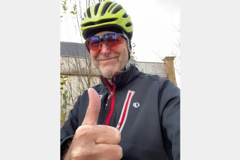 Cancer patient wearing a yellow bike helmet giving the thumb's up