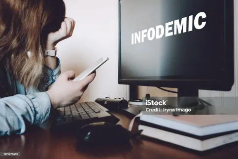 White woman holding her forehead in front of a computer screen that reads "infodemic".