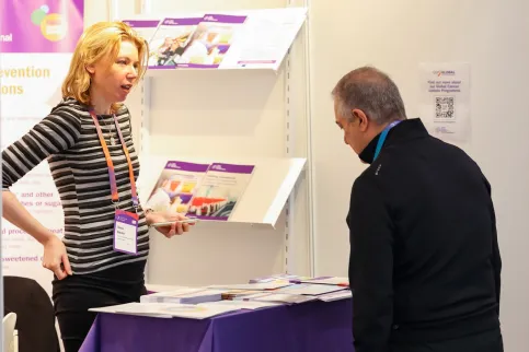 A woman at the booth of the World Cancer Research Fund at the World Cancer Congress speaking to an interested man.