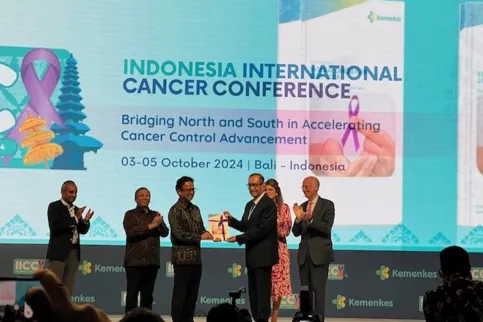 Two Asian men in suits receiving an award on stage at a cancer conference in Indonesia
