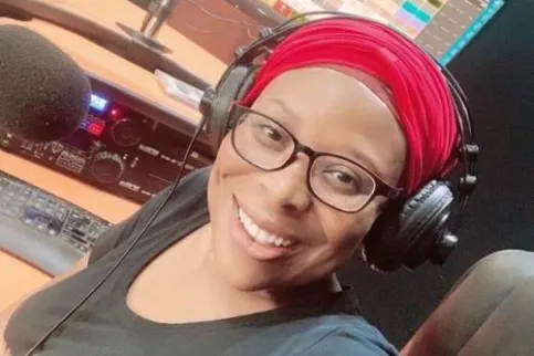 Black woman with red headscarf and wearing headphones smiles to the camera