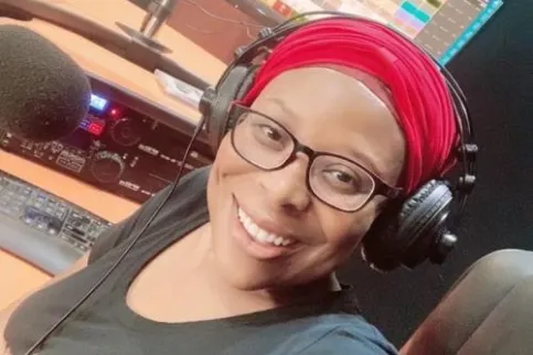 Black woman with red headscarf and wearing headphones smiles to the camera