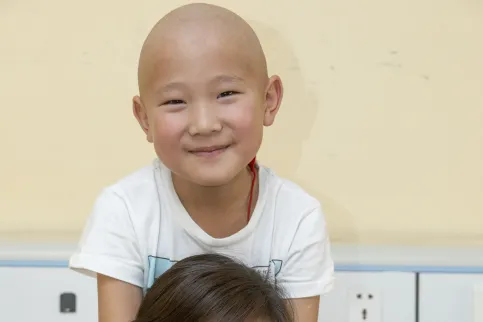 Woman with dark hair in Mongolia with a bald child, cancer patient, on her shoulders
