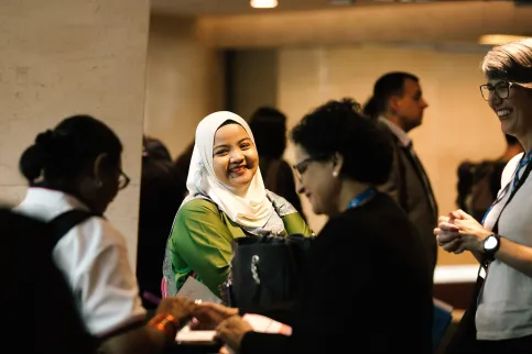 Several people at an event in discussion, focus on a woman wearing a headscarf