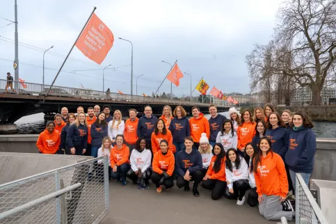UICC staff in blue, white, and orange World Cancer Day 'United by Unique' hoodies in front of a bridge with World Cancer Day flags