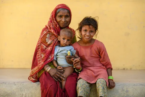 Older Nepalese woman with headdress holding a baby on her knees, a young girl at her side