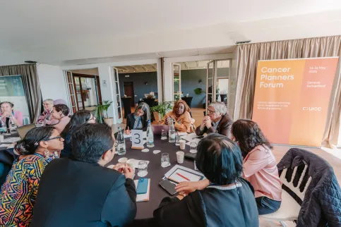 Diverse group of people at a professional seminar around a table, "Cancer Planners Forum" on a banner in the background