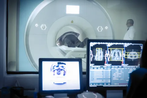 In the background, man having a CT scan. In foreground, computer screens displaying the scans.