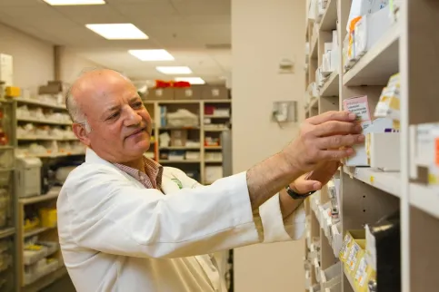 Older white male wearing white lab coat taking medicine from a shelf