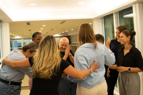 Diverse group of people huddling in a group, one woman without hair clapping