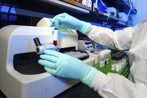 Close up of gloved hands of a lab clinician handling a blood test