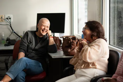 Female cancer patient with no hair laughing as she speaks to another woman on a couch