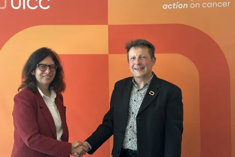 Middle-aged White man and woman shaking hands in front of an orange coloured branded background