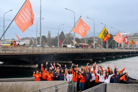 Diverse group of people in branded World Cancer Day sweatshirts standing before the Mont Blanc bridge in Geneva flying World Cancer Day flags