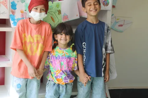 Three children in colorful shirts, one wearing a mask, in a cancer centre for children