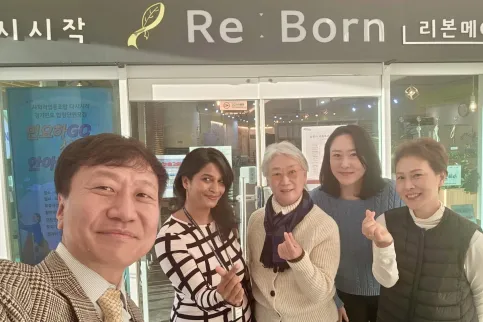 Diverse group featuring one man and four women posing for a picture in front of a sign "Re:Born"
