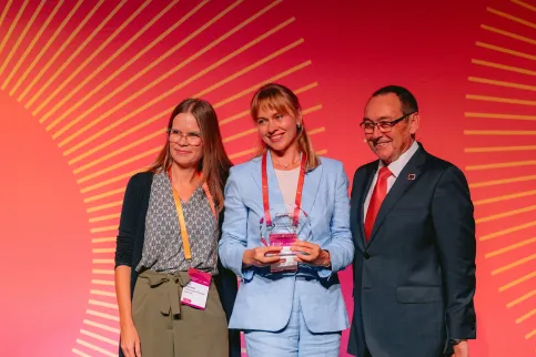 Two women and a man in suit receiving an award on stage
