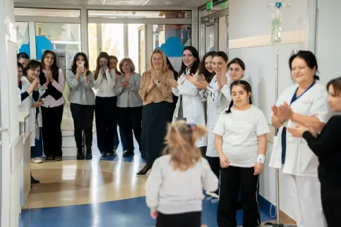 A child with cancer is cheered by the clinicians and health workers as she walks down the hall to ring the remission bell