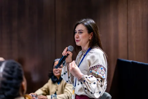 Eastern European woman with black hair speaking into a microphone at a conference.