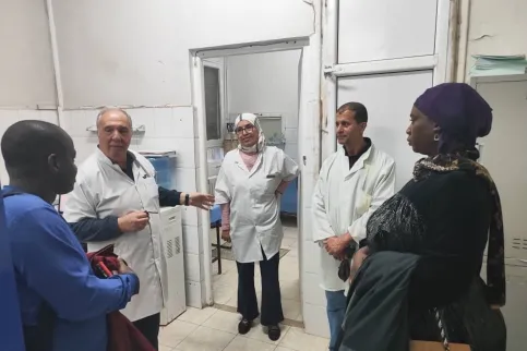 A group of five Middle Eastern and African men and women in hospital setting, 3 in white lab coats, one in blue lab coat, and one women in traditional African dress